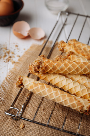 Homemade wafer rolls with nuts on a cooling rack with baking ingredients, rustic setup