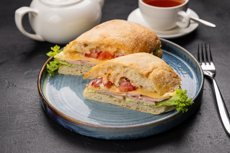 Ciabatta sandwich with cheese, ham and lettuce served with tea on a rustic black backgroundの写真素材