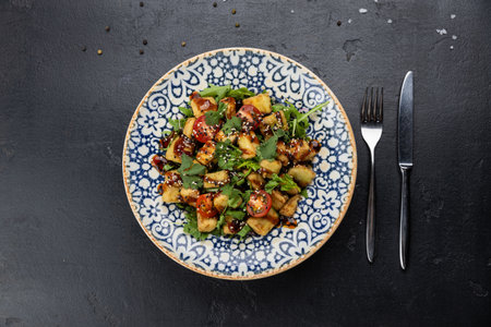 Crispy eggplant salad with cherry tomatoes, herbs and sesame sauce in patterned bowl