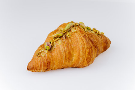 Golden croissant topped with chopped pistachios on white background, gourmet bakery dessertの写真素材