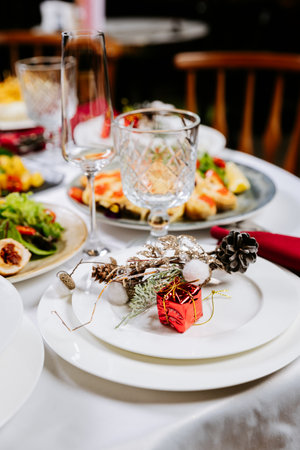 Elegant festive table setting with Christmas decor, white plates, and red gift accentの写真素材
