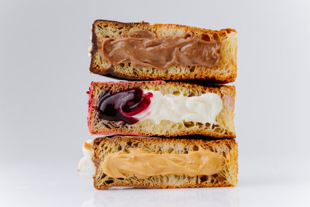 Stack of filled croissant halves with chocolate, cherry and caramel cream on white background