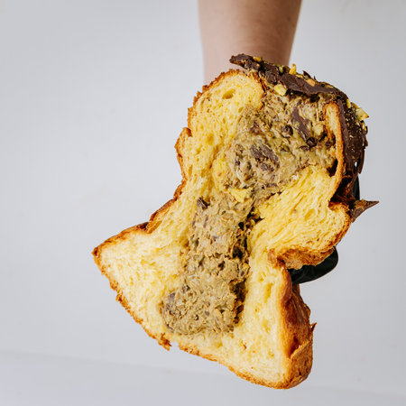 Hand holding sliced nut cream filled Christmas panettone, festive artisan dessert