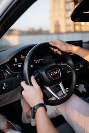 Person driving modern car at sunset, closeup of hands on steering wheelの写真素材