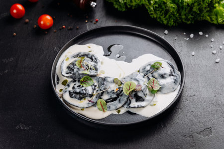 Black ravioli in creamy white sauce with microgreens, gourmet plating on dark slateの写真素材