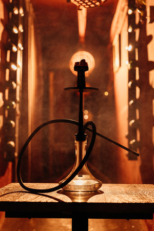 Silhouette of a hookah on a wooden table under warm bar lights, moody lounge atmosphereの写真素材