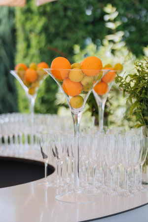 Tall martini centerpiece with citrus above rows of champagne flutes at an outdoor barの写真素材