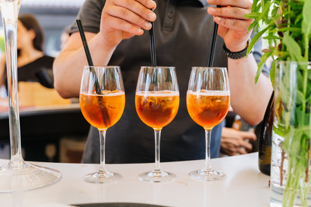 Bartender stirring three Aperol Spritz cocktails in wine glasses at the barの写真素材