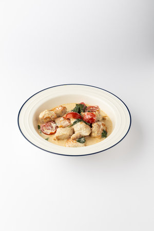 Creamy chicken with cherry tomatoes and spinach in a bowl on white backgroundの写真素材