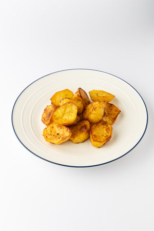 Golden roasted potato chunks on a plate, crispy and seasoned, isolated on whiteの写真素材