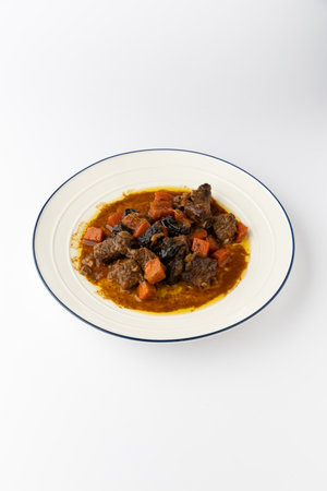 Beef stew with carrots and prunes in rich gravy, served on plate, isolated on whiteの写真素材