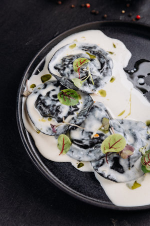 Black ravioli in creamy white sauce with microgreens, gourmet plating on dark slateの写真素材