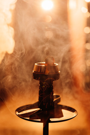 Hookah bowl with glowing coal and drifting smoke in warm bokeh bar lightの写真素材