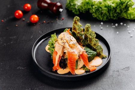 Smoked salmon salad with poached egg, hollandaise and spinach waffles on black plateの写真素材