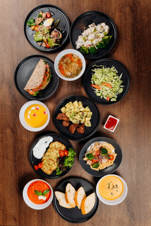 Overhead flat lay of assorted restaurant dishes, soups and salads on wooden tableの写真素材