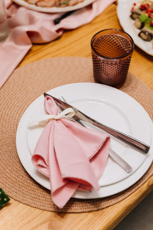 Elegant place setting with pink napkin and ribbon on woven placemat, wedding dinner decorの写真素材