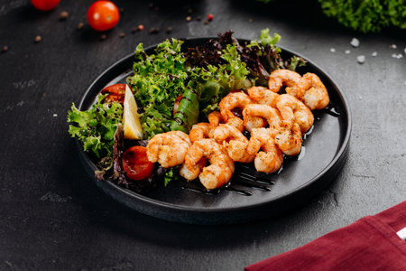 Grilled shrimp salad with mixed greens, cherry tomatoes and lemon on a black plateの写真素材