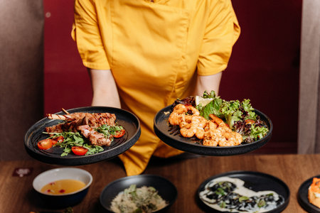 Chef presenting shrimp salad and grilled ribs on black plates in a modern restaurantの写真素材