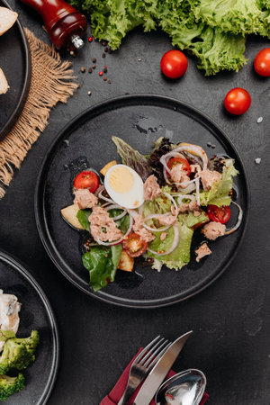 Tuna salad with egg, tomatoes and greens on black plate, restaurant lunch closeupの写真素材