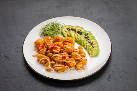 Crispy shrimp bites with spicy mayo, avocado slices and microgreens on a white plateの写真素材