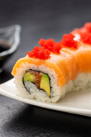 Salmon sushi roll with red roe on white plate, soy sauce, wasabi and ginger, top viewの写真素材