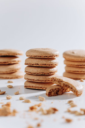 Stacked peanut macarons with bitten cookie and crumbs on white backgroundの写真素材