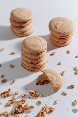 Stacked peanut macarons with bitten cookie and crumbs on white background