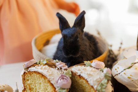 Black baby bunny with sliced Easter cake and festive spring dessert tableの写真素材