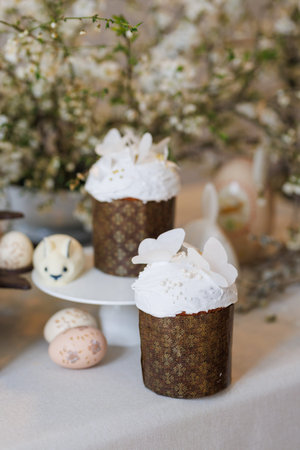 Easter cake on stand with painted eggs and bunny treat, spring blossom background, soft light