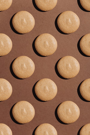 Seamless pattern of beige macarons with hard shadows on brown backgroundの写真素材