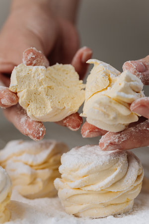 Hands breaking vanilla zephyr with powdered sugar, close-up homemade dessertの写真素材