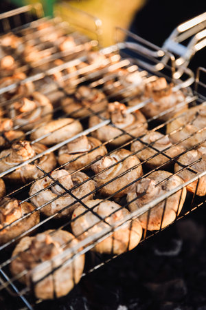 Closeup of mushrooms grilling on barbecue grate with warm summer light and shallow depthの写真素材