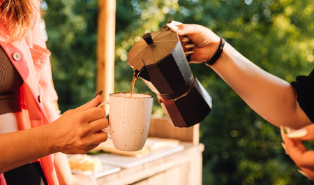 Moka pot pouring hot coffee into mug outdoors at sunsetの写真素材