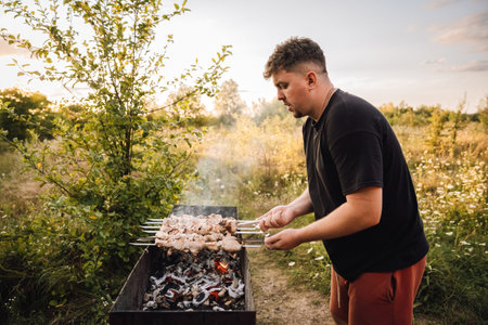 Man grilling pork shashlik over charcoal in countryside at sunsetの写真素材