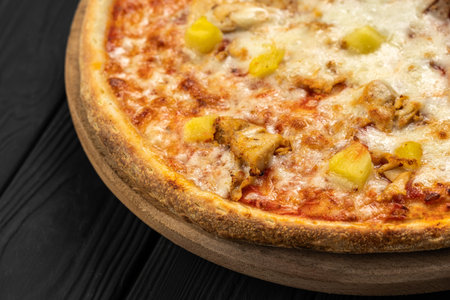 Chicken pineapple pizza with melted mozzarella on wooden board, dark backgroundの写真素材