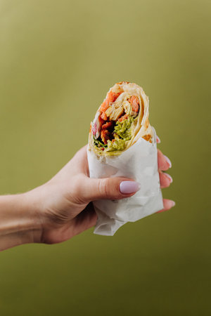 Hand holding grilled salmon wrap with avocado sauce on green backgroundの写真素材