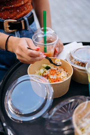 Hands eating poke bowl with takeaway drinks, street food lunch