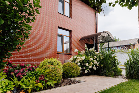 Brick house side entrance with canopy and landscaped flower bed, hydrangeas and shrubsの写真素材