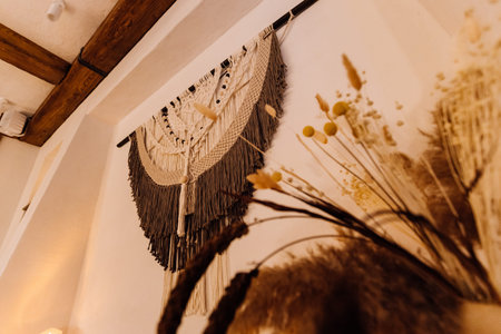Boho macrame wall hanging with candles and dried flowers on rustic shelf