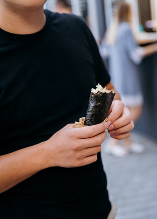 Close up of person holding sushi hand roll street food snack outdoors