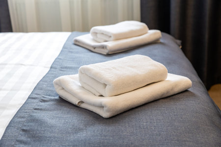 Folded white towels on hotel bed close up with clean modern hospitality interior