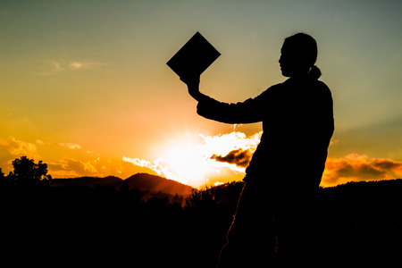 silhouette of a woman holding up a bookの写真素材