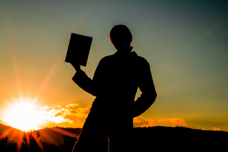 silhouette of a woman holding up a bookの写真素材