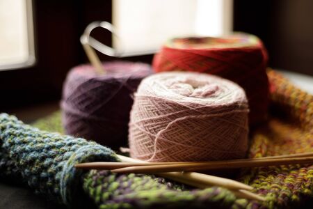 Woolen yarn for knitting. Pink, red, purple balls of natural wool yarn and wooden knitting needles lie on a colorful yellow-red knitwear. Close-up, blurred background.の写真素材