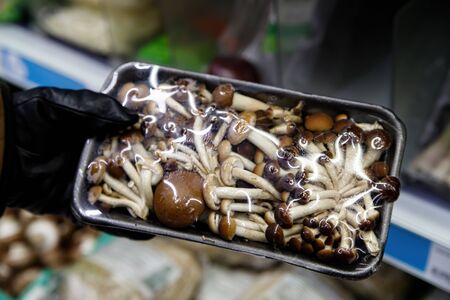 A man's hand holds a plastic bag of mushrooms in a grocery store. Plastic product packaging.の写真素材