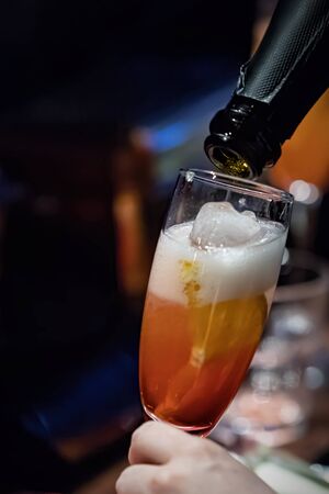 Pouring the champagne the orange puree to make a cocktail alcoholic drink. Selective focus. A bottle of champagne pours wine into a glass, close-upの写真素材