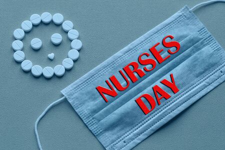 White tablets are arranged in the form of a smiley face on a yellow background. Text of congratulations on the medical holiday nurse's Day. Healthcare and medical conceptの写真素材