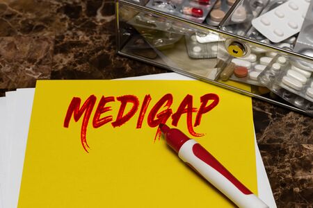 Medigap is written in red letters on a yellow sheet lying on the table next to a box of pills. Medical or healthcare conceptの写真素材