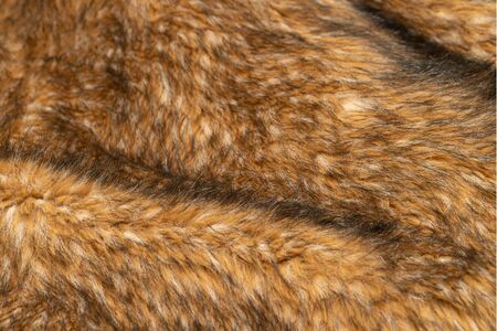 Close-up of a fluffy dark brown faux fur fabric with a background texture. Brown artificial fabric,...