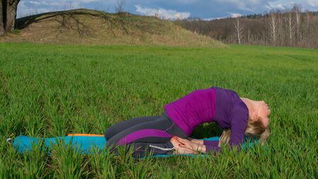 A middle-aged blonde woman in a tracksuit practices yoga outdoors. Healthy lifestyle and Slow life...